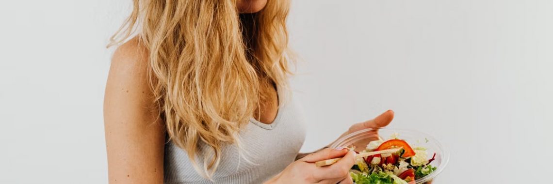 A caucasian woman in a sports bra enjoying a fresh salad, embodying healthy eating and lifestyle.